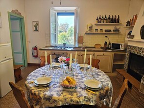 A dining room with a round table set for six, a kitchen in the background, and a fireplace.