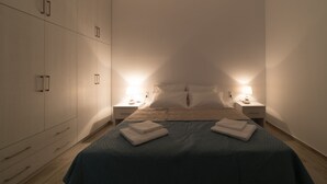 Un dormitorio con una cama, dos mesitas de noche, un armario y una mesita con lámparas.