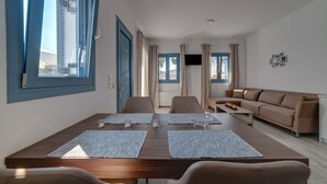 Una sala de estar moderna con una mesa de comedor de madera, un sofá color beige y un televisor montado en la pared.