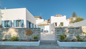Una calle estrecha con edificios blancos, muros de piedra y un letrero que dice 'Gina's House'.