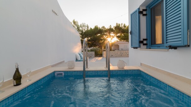 Una piscina con agua azul cristalina, una botella de vino y una copa al borde.