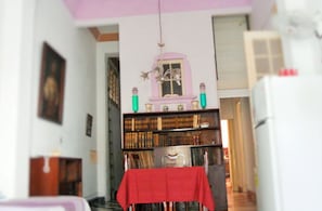 Ein Zimmer mit Bücherregal, einem Tisch mit rotem Tischlein und einer Pendelleuchte.