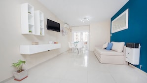 A modern living room with a white sofa, a TV mounted on the wall, and a dining area in the background. - Rent Corro X32 (Córdoba)