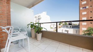 Un balcon avec des chaises blanches, deux plantes en pot et une vue sur les bâtiments environnants.