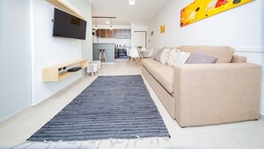 Un salon moderne avec un canapé, un téléviseur à écran plat et une cuisine en arrière-plan.