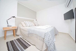A bedroom with a bed, bedside table, lamp, TV, and a striped rug.