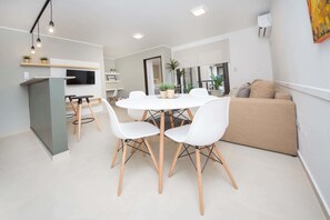A modern living room with a round dining table, white chairs, a beige sofa, and a TV mounted on the wall. - Rent San José de Calasanz CX5 (Córdoba)