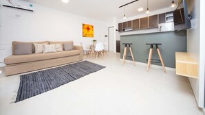 Ein modernes Wohnzimmer mit Sofa, Esstisch und Küchenzeile mit Hockern.