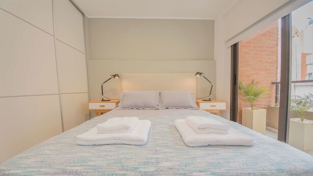 A modern hotel room with a large bed, two bedside tables with lamps, a view of the outside through a glass door, and a small potted plant on the windowsill. - Rent San José de Calasanz WH5 (Córdoba)