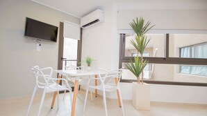 A modern dining area with a white table and chairs, a mounted TV, an air conditioning unit, and a large window with a view. - Rent San José de Calasanz WH5 (Córdoba)