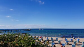 A beach with rows of blue and white beach chairs, a pier extending into the sea, and sailboats in the distance.