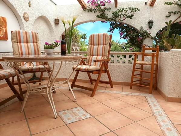 A patio area with a round table and striped chairs, a small vase with flowers, and a cactus plant.