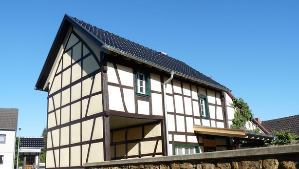 Ein traditionelles Fachwerkhäuschen mit Bruchstein-Fundament, einem steilen Walmdach und einer kleinen Veranda.