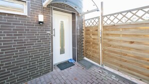 Facade i mursten med en hvid dør, et træhegn og et metalmarkise.