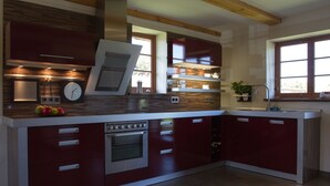 A modern kitchen with red cabinetry, a built-in oven, and a clock on the wall. - Cottage on the Bay of Greifswald between the sun islands of Rügen and Usedom (Ludwigsburg)