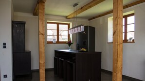 A modern kitchen with dark cabinetry, a central island, wooden beams, and large windows. - Cottage on the Bay of Greifswald between the sun islands of Rügen and Usedom (Ludwigsburg)