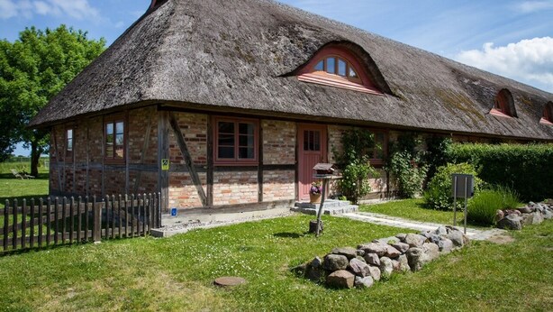A traditional stone house with a thatched roof, wooden windows, and a small garden area with a wooden fence and rocks. - Cottage on the Bay of Greifswald between the sun islands of Rügen and Usedom (Ludwigsburg)