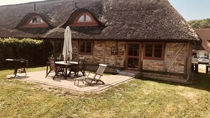 A rustic building with a thatched roof, a brick exterior, and a patio area with a table and chairs. - Cottage on the Bay of Greifswald between the sun islands of Rügen and Usedom (Ludwigsburg)