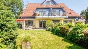 A two-story house with a red-tiled roof, a balcony with a yellow umbrella, and a well-maintained garden. - Comfortable, quiet 3-room first floor apartment, garden, fireplace and underfloor heating (Mecklenburg-Vorpommern)