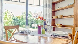 A wooden dining table with a view of a garden through large windows. - Comfortable, quiet 3-room first floor apartment, garden, fireplace and underfloor heating (Mecklenburg-Vorpommern)