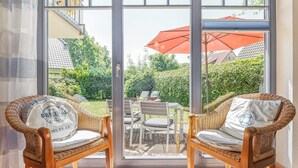 Two wicker chairs with cushions and a glass door leading to an outdoor patio with a table and chairs, and a red umbrella. - Comfortable, quiet 3-room first floor apartment, garden, fireplace and underfloor heating (Mecklenburg-Vorpommern)