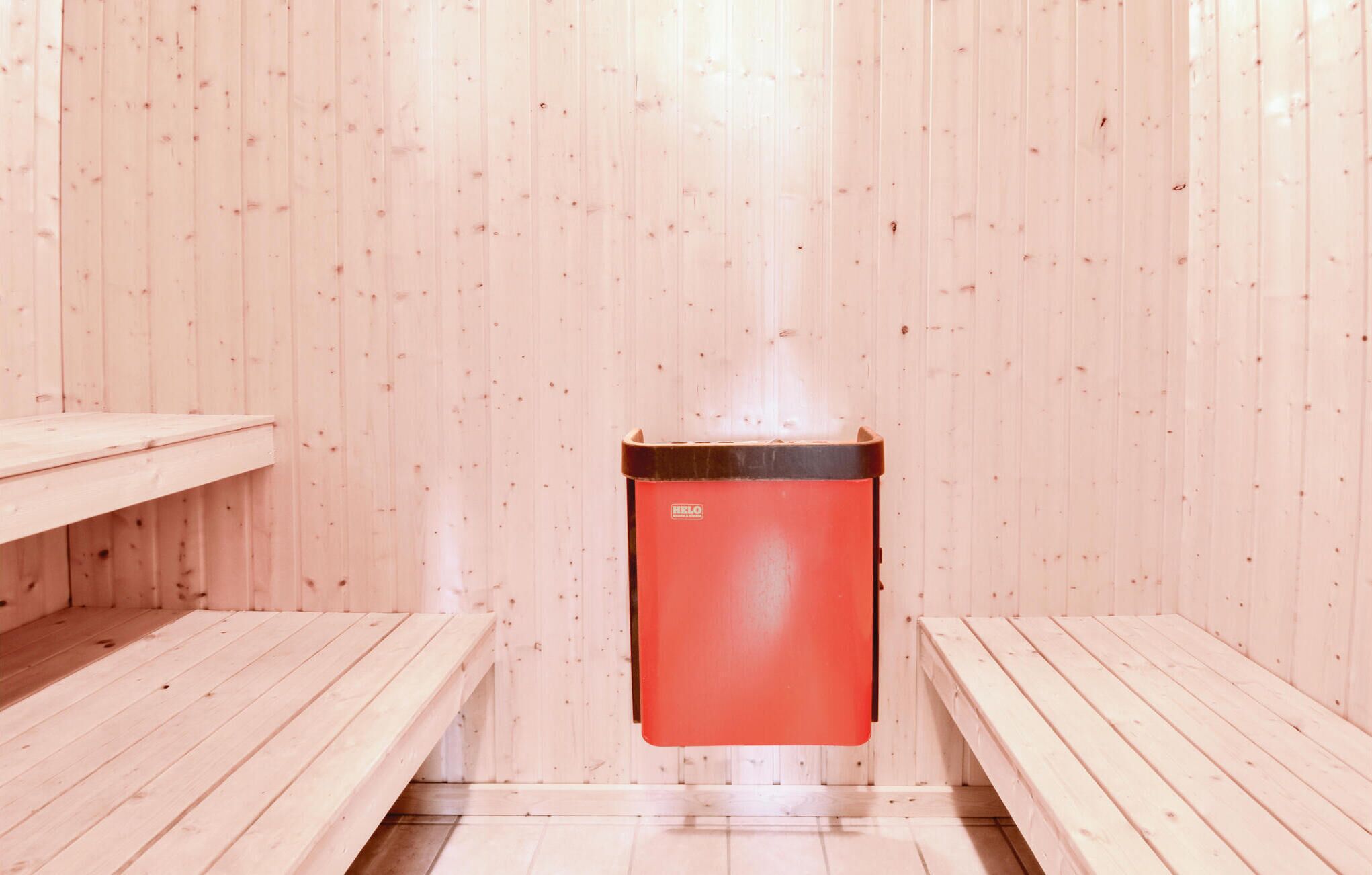 Una sauna con bancos de madera y un calentador rojo.