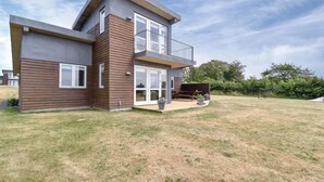 Una casa moderna de dos pisos con fachada de madera, ventanas grandes y una terraza con mobiliario exterior.