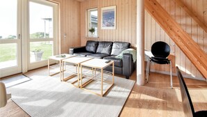 Una sala de estar moderna con detalles de madera, un sofá de cuero negro, una mesa de centro blanca y vistas al exterior a través de amplios ventanales.