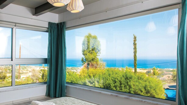 A bedroom with a large window offering a view of the sea and greenery.