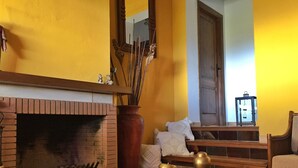 A room with a brick fireplace, a wooden table with decorative items, a large vase, and a chair.