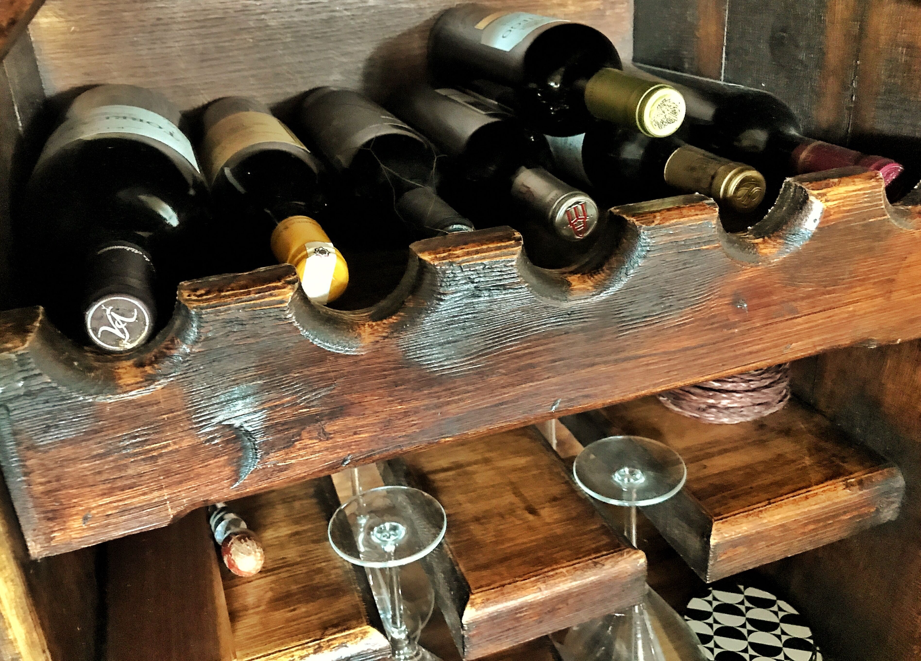 A wooden wine rack holding several wine bottles and glasses.