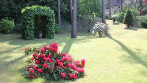 En velplejet have med forskellige buske og blomster, herunder en markant busk med røde blomster i forgrunden.