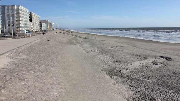 En strandpromenade med en række høje bygninger, en sandstrand og havet.