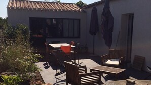 Une terrasse avec des meubles d’extérieur, un mur en pierre et un bâtiment blanc doté d’un toit en tuiles.