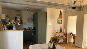 Une cuisine moderne dotée d’un îlot central, un coin repas avec une nappe à motifs et un espace de vie agrémenté d’une bibliothèque et d’objets décoratifs.