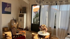 Un salon chaleureux avec un canapé rouge, des fauteuils en osier, une petite table ronde ornée d’un vase et un lustre.