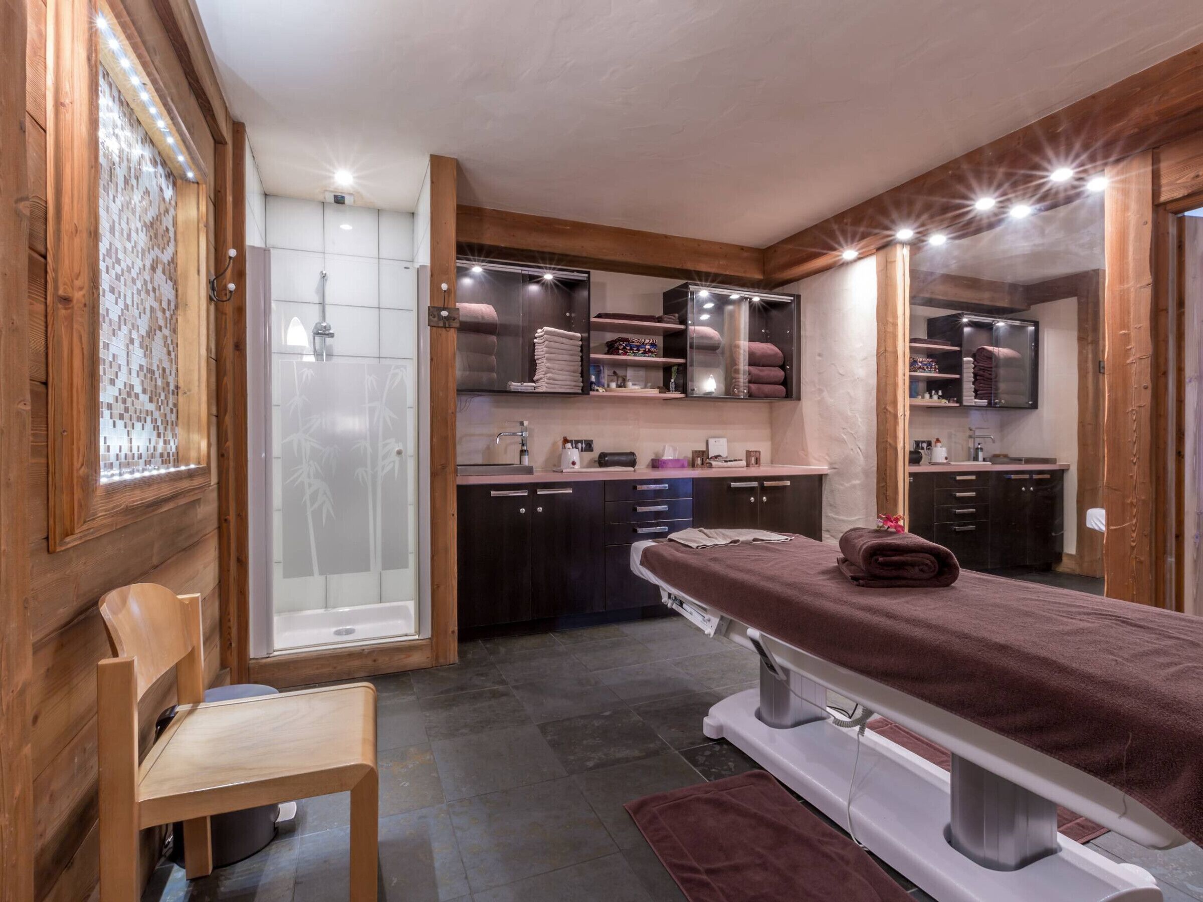 A spa room with a wooden interior, a massage table, a shower area, and a small seating area.