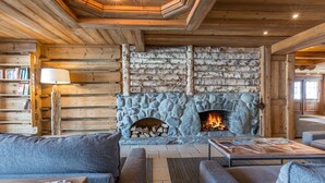 A cozy log cabin interior with a stone fireplace, a sofa, a coffee table, and a bookshelf. - 3-bedroom chalet with spa and pool, ski-in/ski-out (Saint-Martin-de-Belleville)