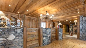 A wooden interior with stone walls, a chandelier, and a reception area with a counter displaying bottles. - Apartment for 6 with pool, spa, parking - Ski-in/Ski-out (Saint-Martin-de-Belleville)