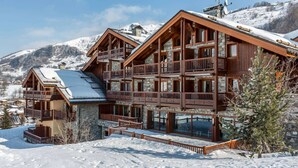 Ein mehrstöckiges Holzchalet mit Balkonen vor einer verschneiten Bergkulisse.
