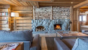 Un acogedor interior de cabaña de madera con chimenea de piedra, paredes de madera y una zona de estar confortable.