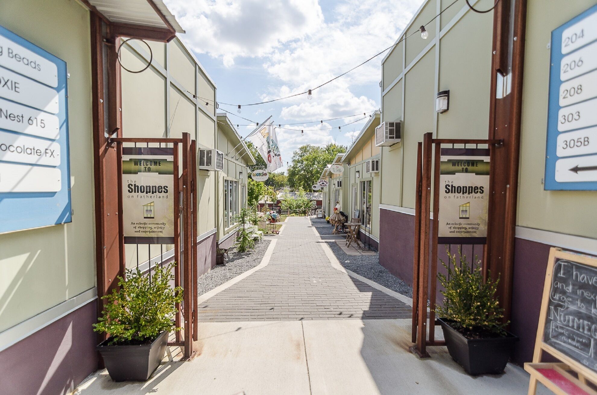 Una estrecha calle peatonal bordeada de tiendas, portones de madera y plantas en macetas.