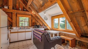 Un intérieur de chalet chaleureux comprenant une cuisine, un coin repas et une chambre en mezzanine avec vue.