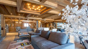 L’intérieur d’un chalet confortable, avec des murs en bois, un canapé d’angle, une table basse avec des magazines et une cheminée.