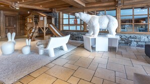 L’intérieur d’une cabane en rondins, avec un mur en pierre, un plafond en bois, une sculpture d’ours polaire et une maison de jeu en bois.
