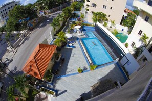 Vue aérienne d’un hôtel avec une piscine, des chaises longues et des palmiers.
