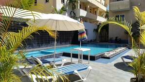 A swimming pool with lounge chairs and umbrellas, surrounded by palm trees and a tiled deck. - Awesome Apartament , Sea View, Swimming pool, In Boca Chica Apt 29 (Boca Chica (santo Domingo))