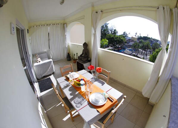 Un balcon avec une table à manger, une statue de Bouddha et une vue sur un quartier résidentiel.