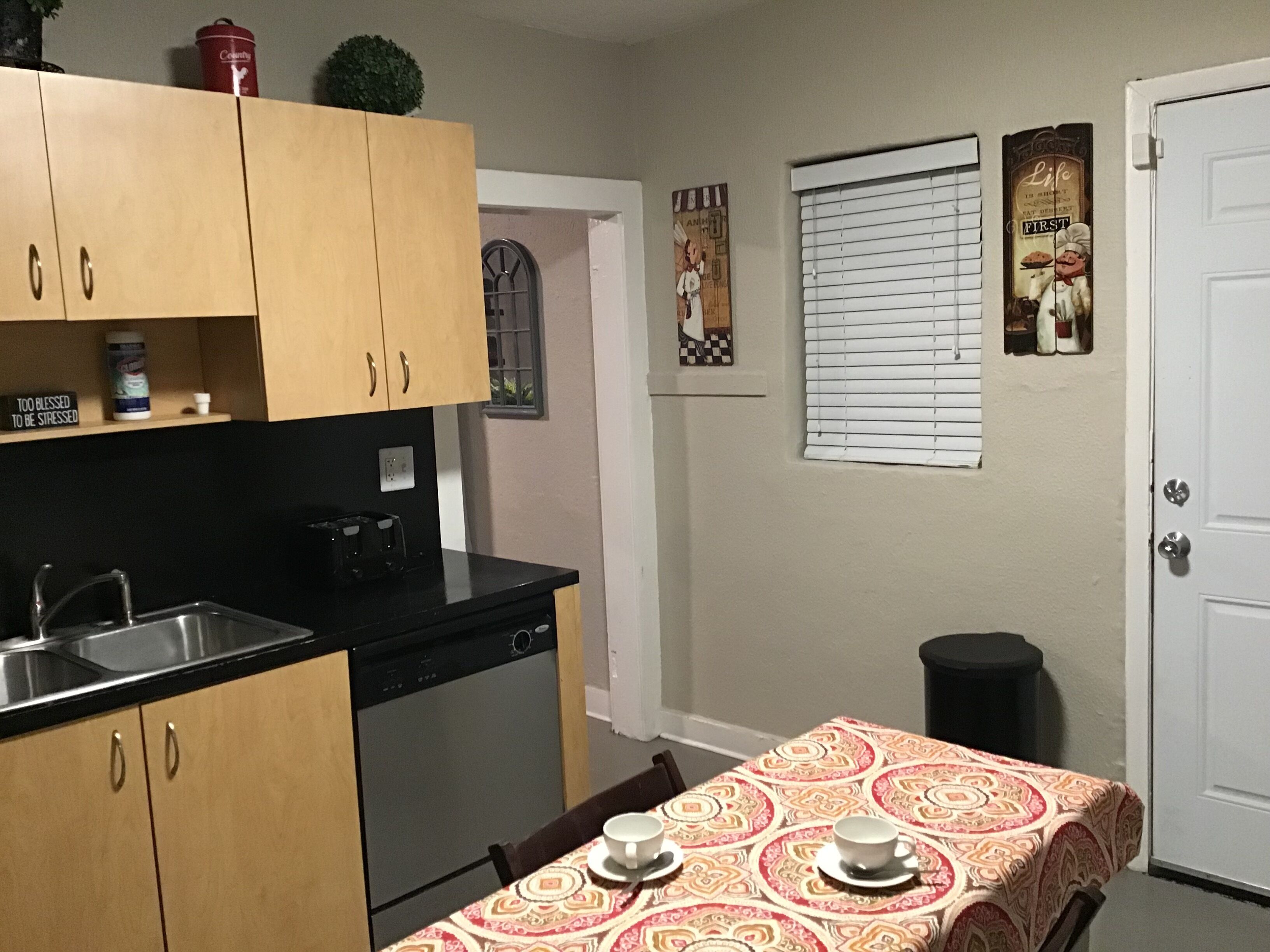 Una cocina funcional con armarios de madera, lavavajillas y una mesa de comedor dispuesta con tazas y platos.