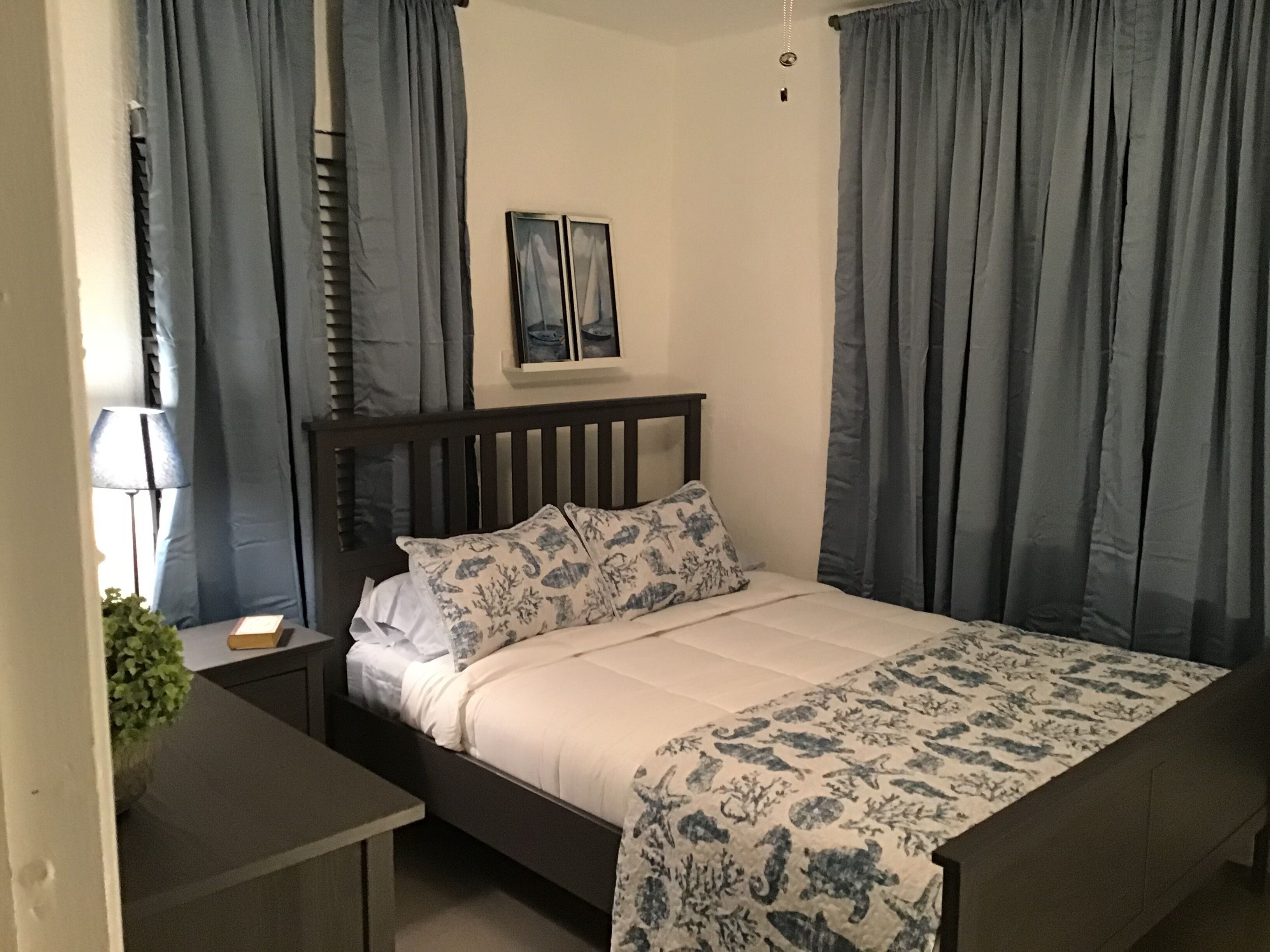 A bedroom with a bed, a nightstand, a lamp, and a window with curtains.